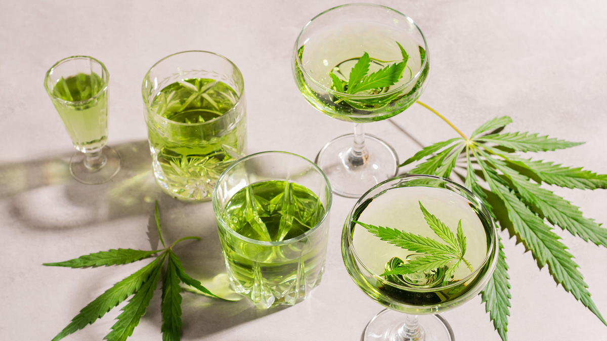 Verschillende glazen lichtgroene drankjes met cannabis, gegarneerd met verse blaadjes op een witte ondergrond
