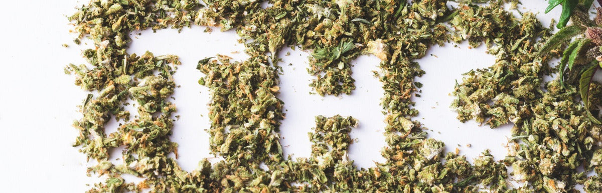 Gedroogde cannabisbloemen op een witte achtergrond met detail van een groen plantenblad
