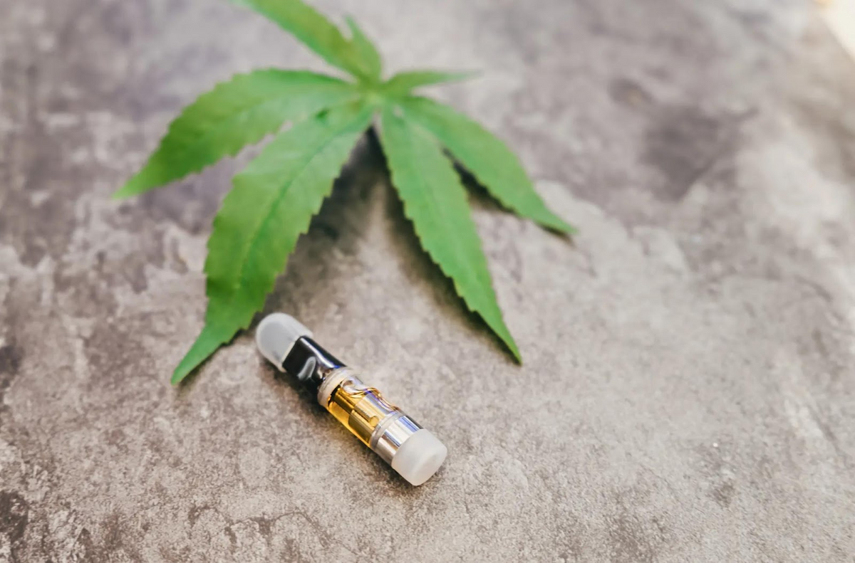 Cannabisblad en vape-cartridge op een betonnen ondergrond