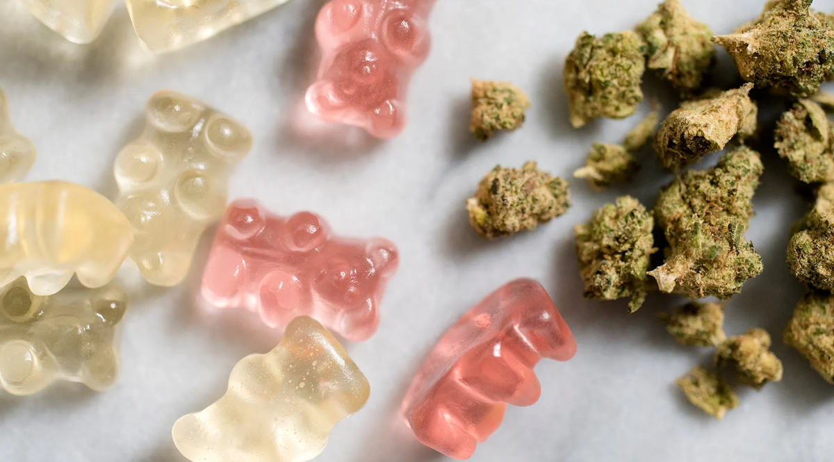 Doorzichtige en roze gummyberen naast cannabistoppen op een witte ondergrond